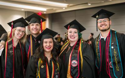 Aims graduates wearing caps and gowns and smiling at the camera 