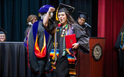 An Aims graduate on stage fist-pumping to celebrate commencement