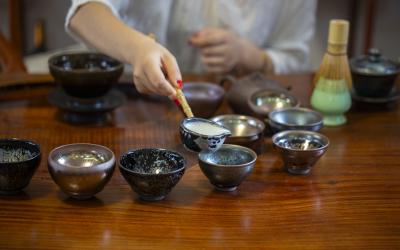 close up of hand holding ladle pouring tea into cups arranged in a half circle 