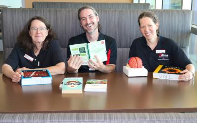 3 Aims TRIO tutors sitting at a table with books in front of them, from left to right: Nike Rovero, Stan Scott, Karen Lehman