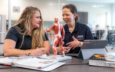a student with long blonde hair sits at a table with advisor with anatomy model on table between them