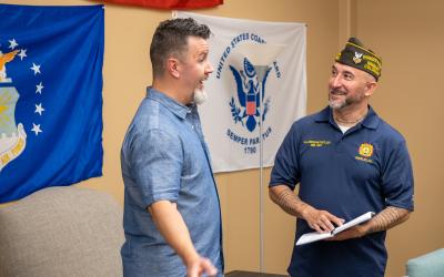Two men in blue shirts talking in front of US military banners