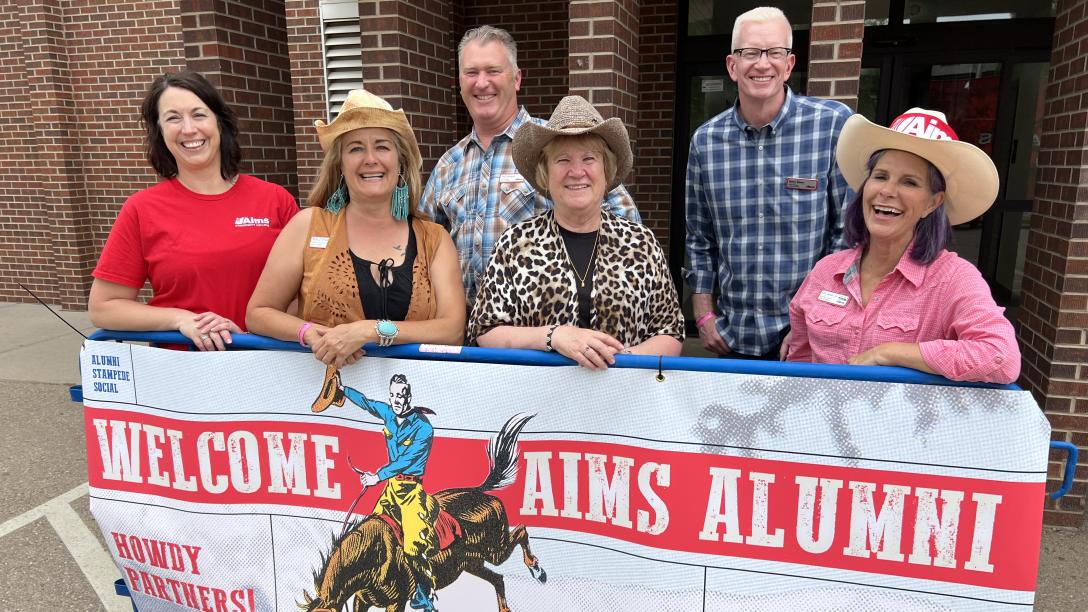 Group standing in front of sign saying, "Welcome Aims Alumni."