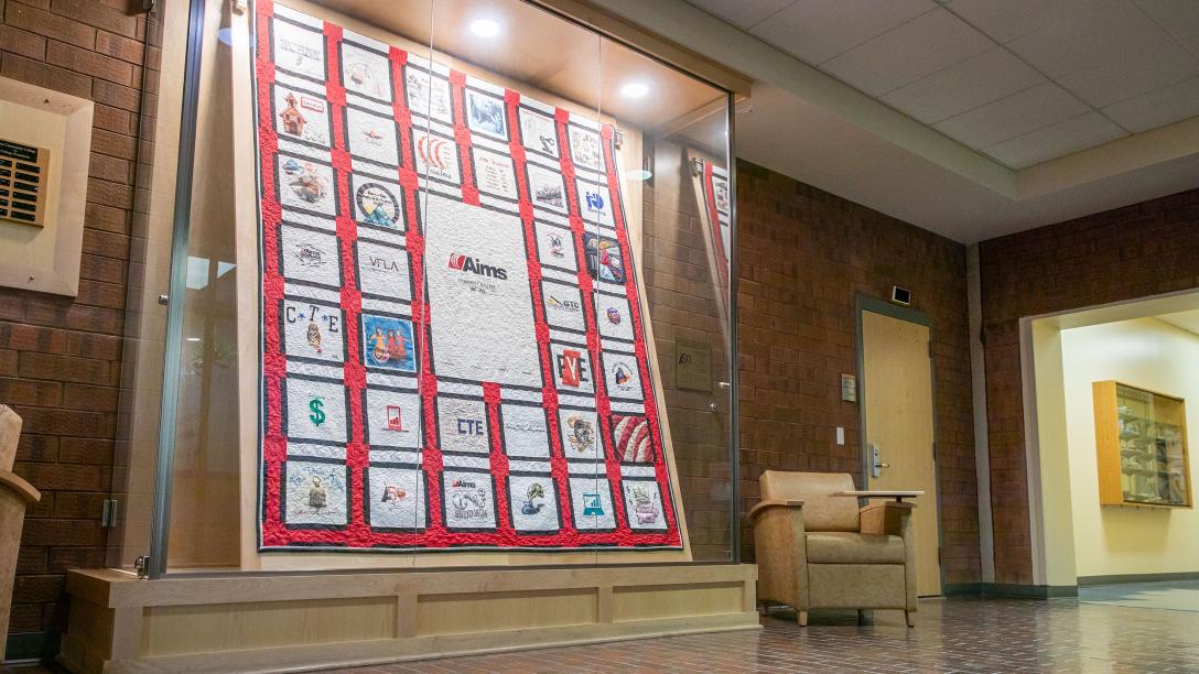 A display case holding a memory quilt featuring the history of Aims Community College.