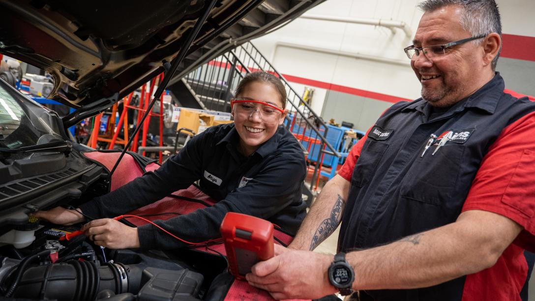 An automotive student is working on a car with her instructor helping.