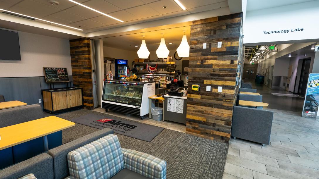 Exterior of Arty's Cafe. A cash register next to a cold food display. Chairs and tables are nearby for use.