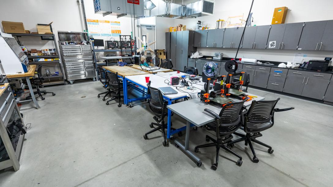 Interior photo of the Community Lab. A large central work area with 3D printers and workstations.