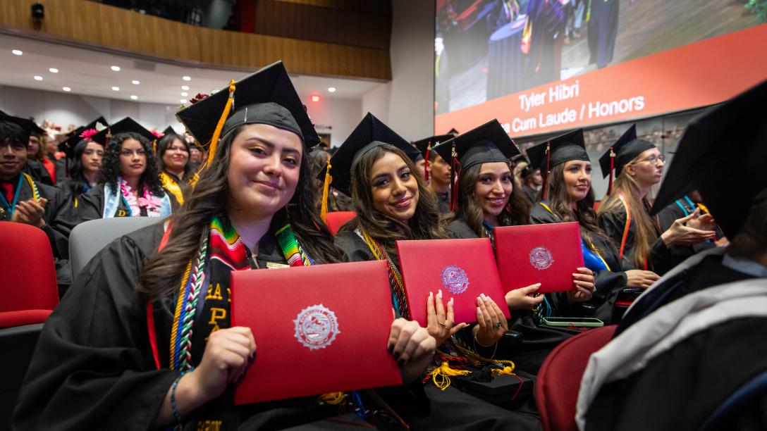 row of aims graduations holding their diplomas