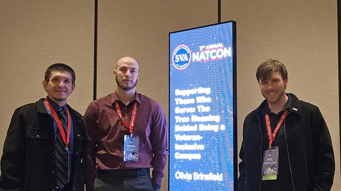 3 men standing next to blue banner with white text that reads "17th Annual NATCON Supporting those who serve the true meaning behind being a veteran inclusive campus"