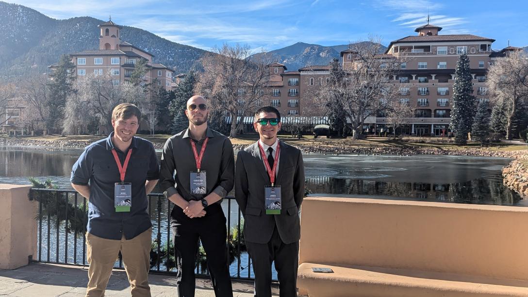 three men outdoors with mountains behind them