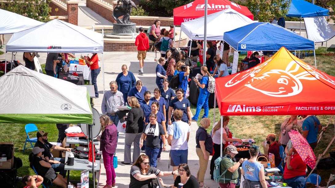 An overhead view of small tents set up outside the Allied Health building. Students are wandering amongst the tents learning about different Aims services and clubs.