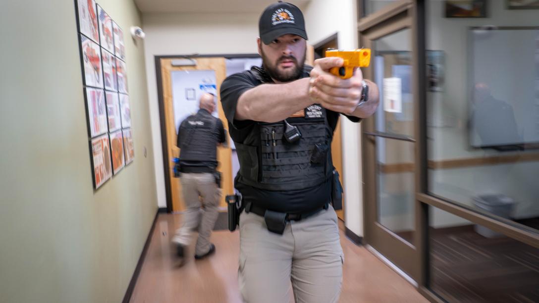 An Aims Peace Officer Academy cadet in action during an active shooter drill, in uniform holding a practice handgun