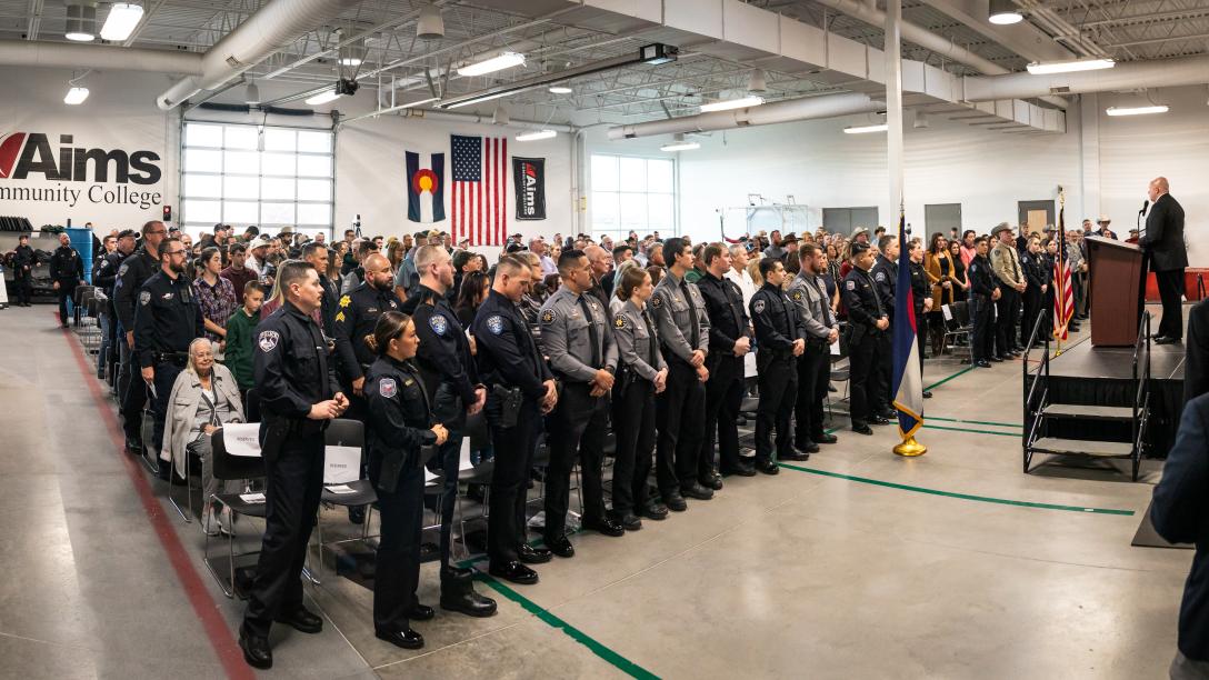 A wide view of an Aims Peace Officer Academy graduation ceremony, with attendees listening to a speaker at the front of the room