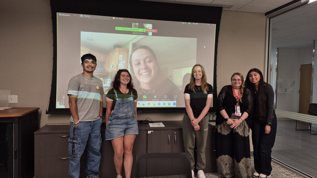 CAP students posing in front of a screen with a Zoom call showing another CAP student.