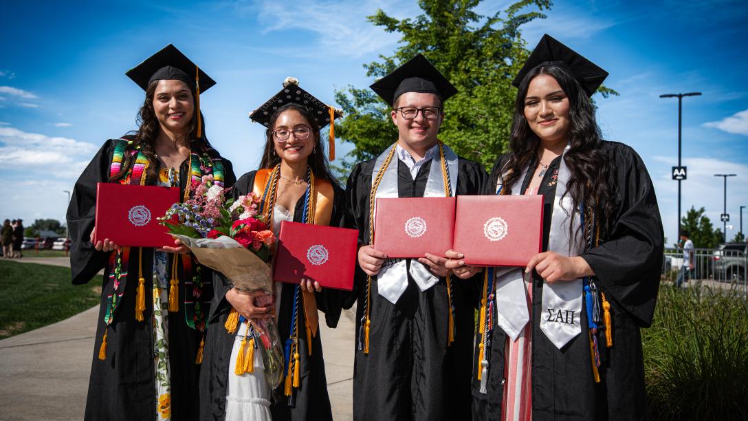 4 students with diplomas after graduation in caps and gowns