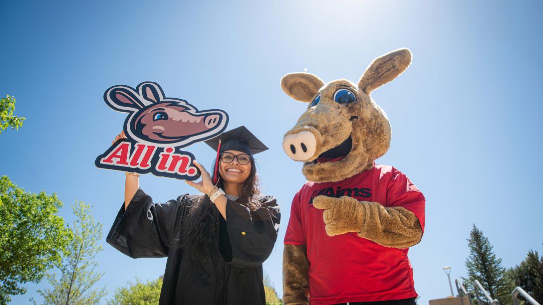Arty and student in cap in gown with "All in" sign