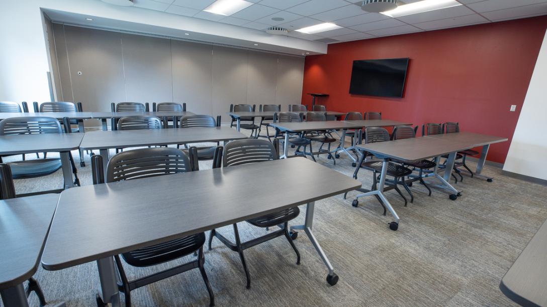 Interior classroom in Summit Building with red wall, gray carpet and several sets of chairs and tables