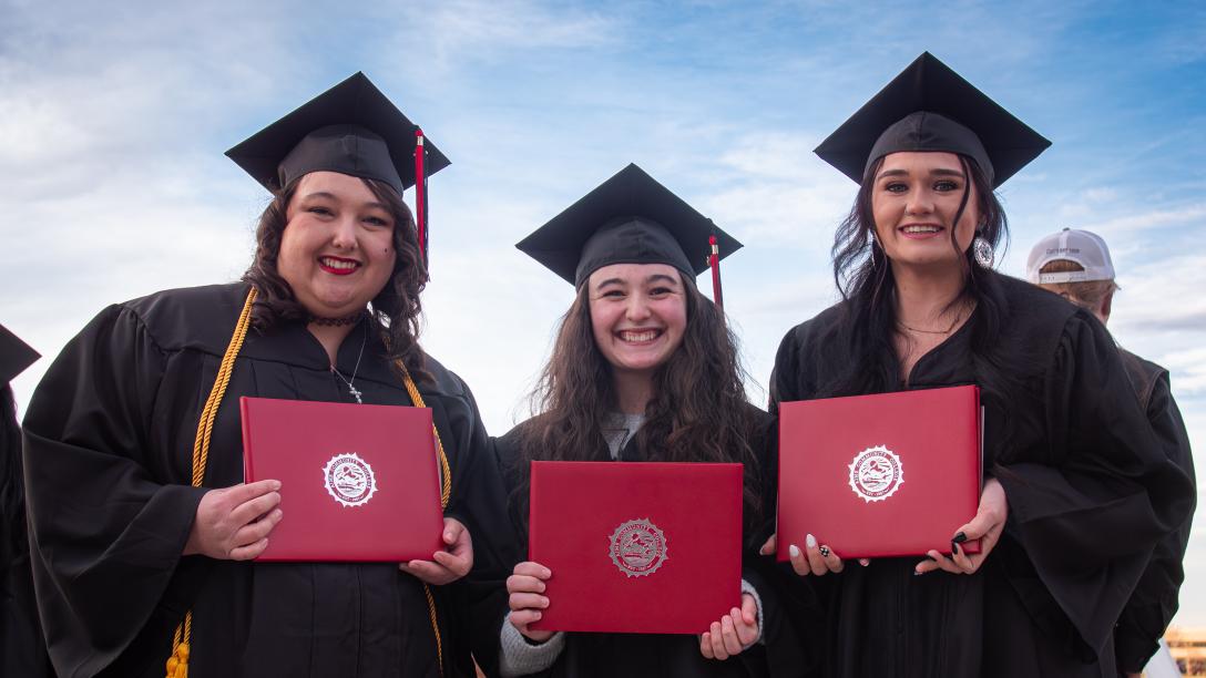 3 females in caps and gowns with diplomas