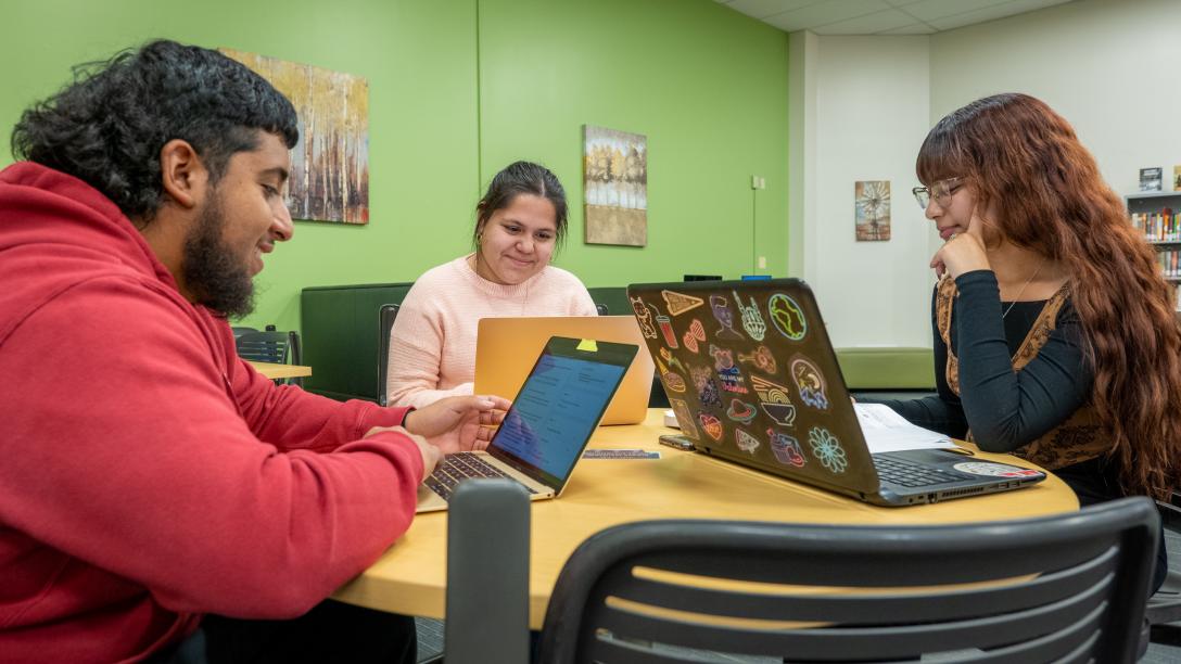 three students studying on laptops at a table