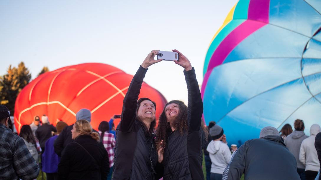 People taking a selfie in front of hot air balloons getting ready for takeoff