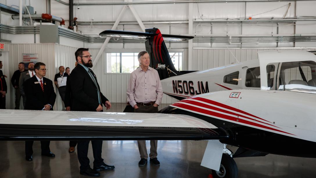 Hickenlooper and Aims staff looks at airplane in hanger