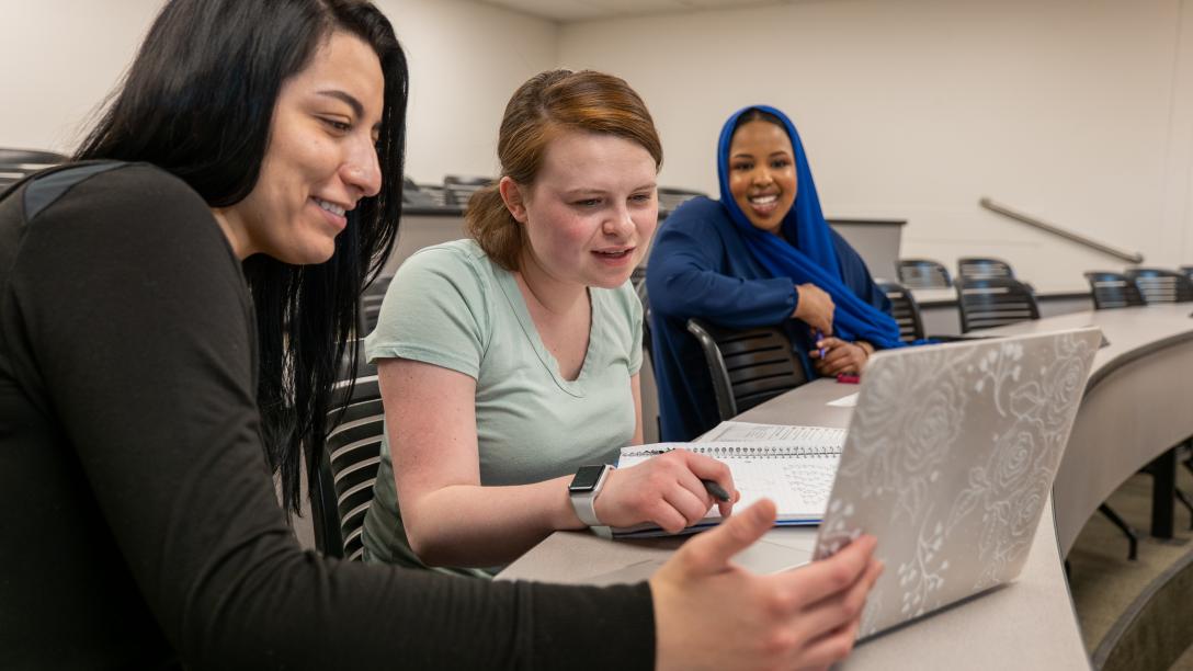 three students looking at a laptop in a classroom