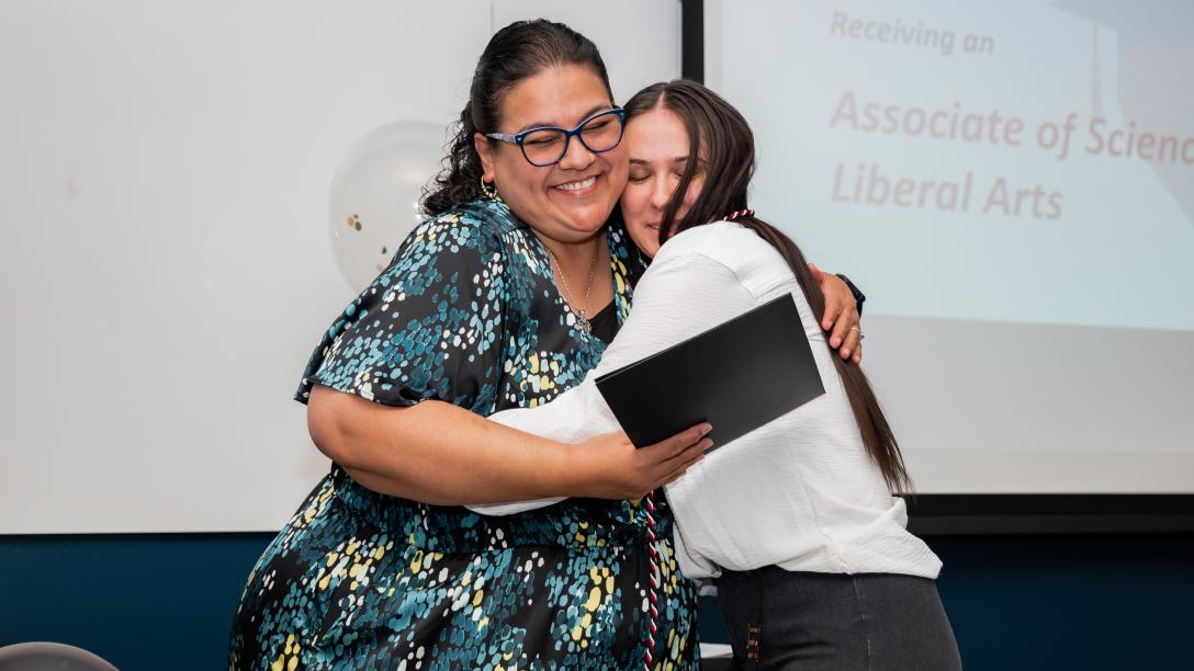 Two women hugging as one receives a certificate
