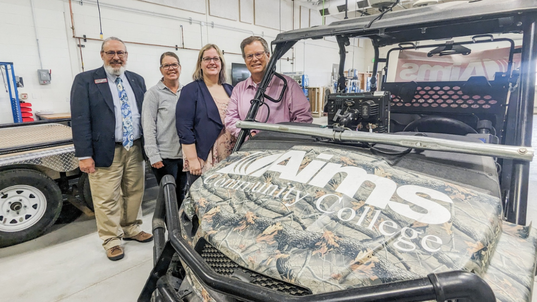Four people posed with camouflaged utility task vehicle