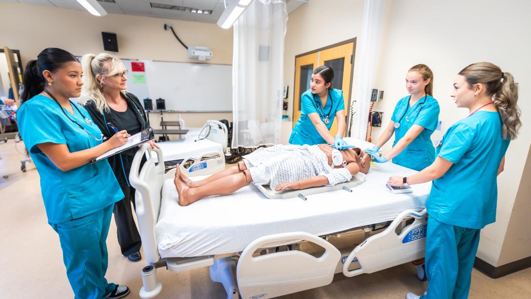 instructor and students standing around a hospital bed with mannequin patient
