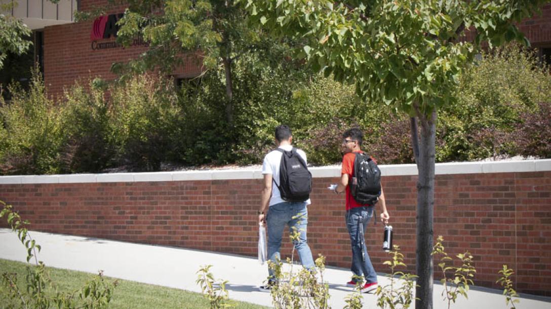 Two students walking on sidewalk next to brick wall