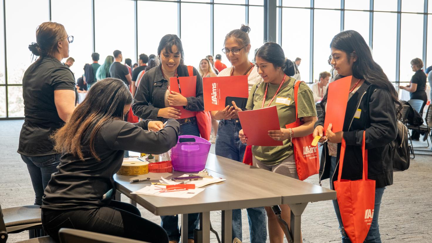 four students standing in front of table talking with seated transition coach on transition day at Aims 2022