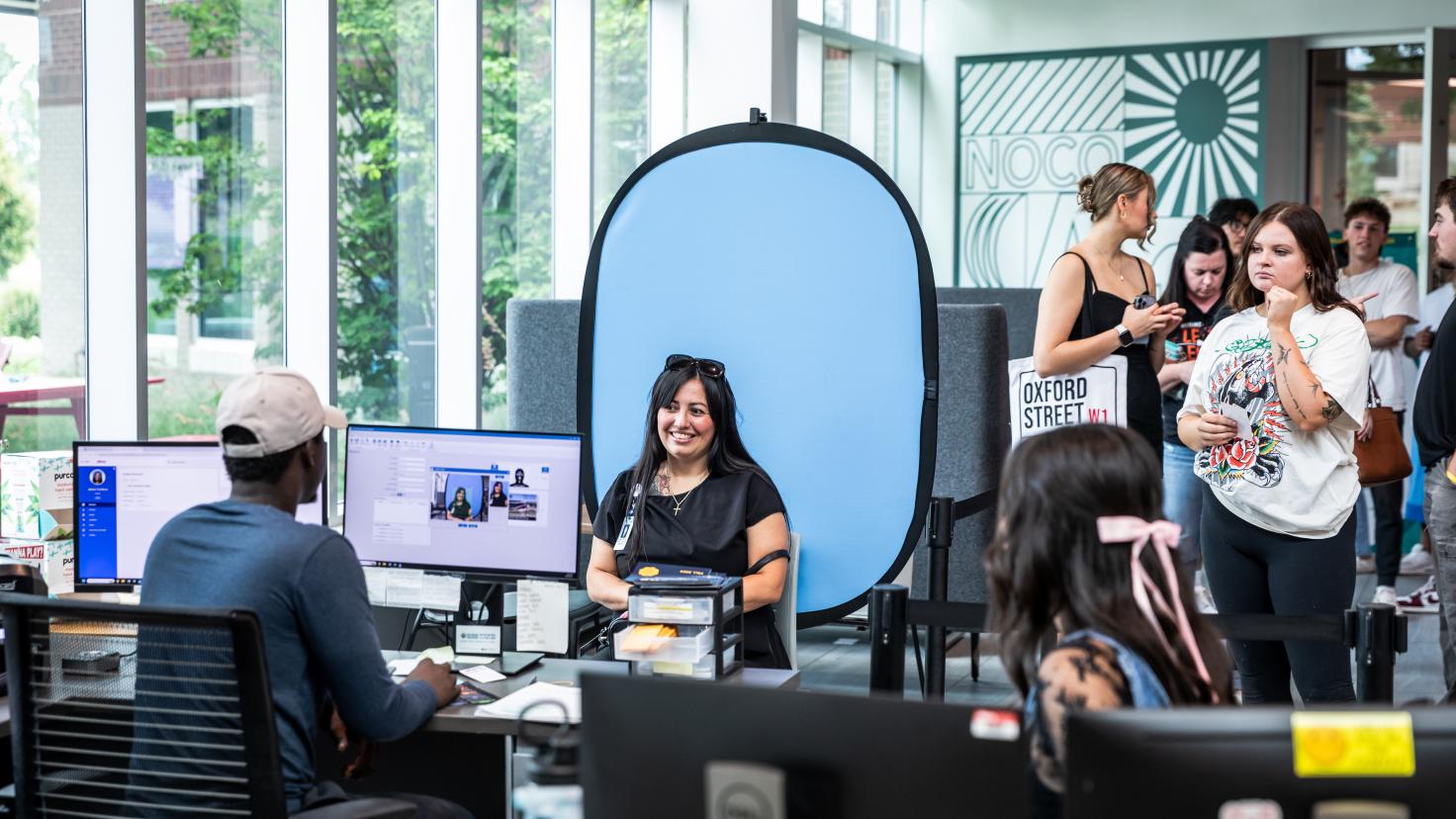 Student sits to have ID photo taken while other students stand in line waiting for their turn