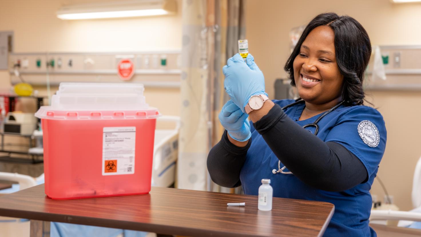 An Aims nursing student practicing using a syringe in a lab classroom