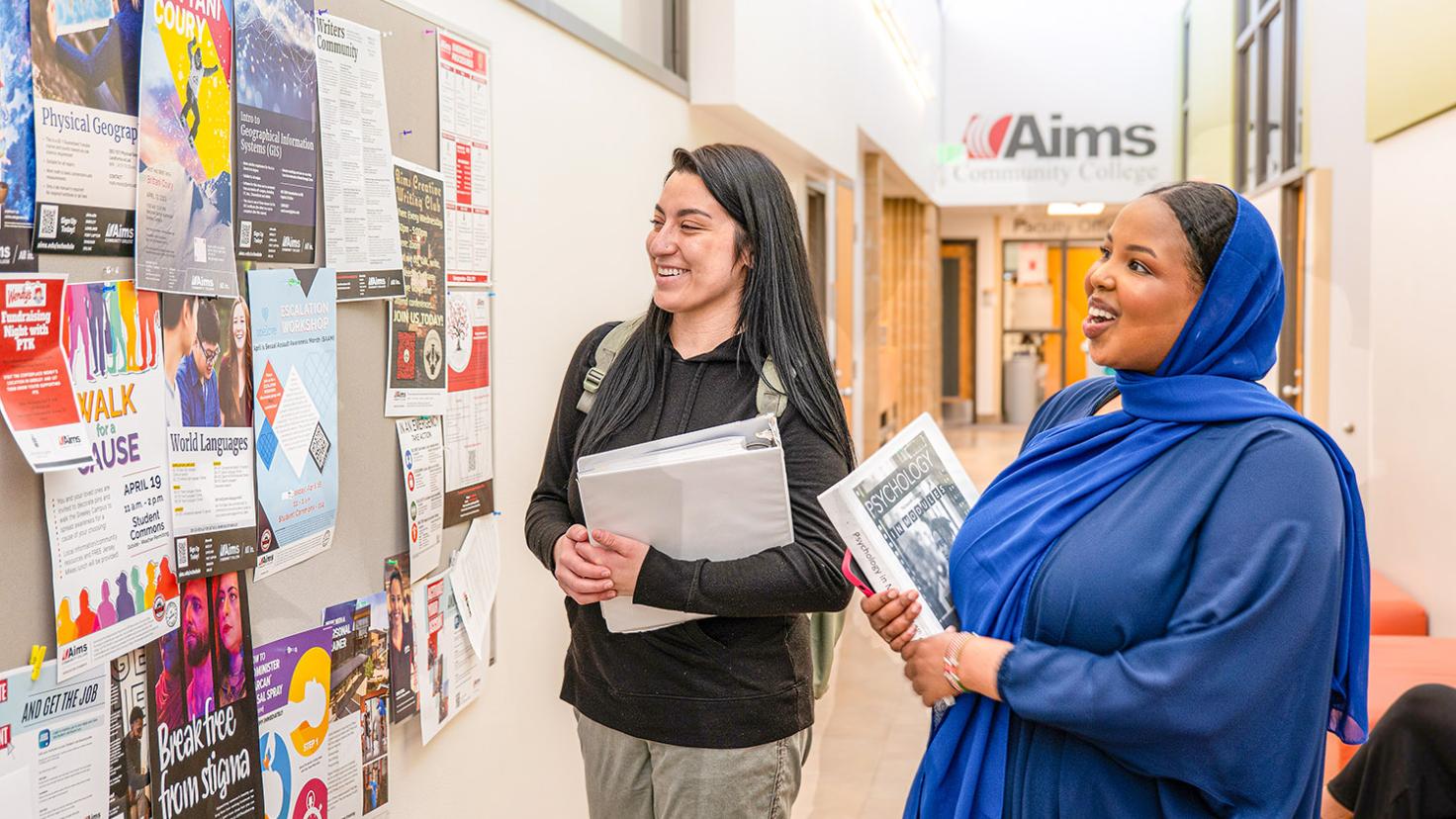 Two students smiling and walking through a brightly lit hallway, two sitting and talking on a bench while three walk by with books and backpacks.