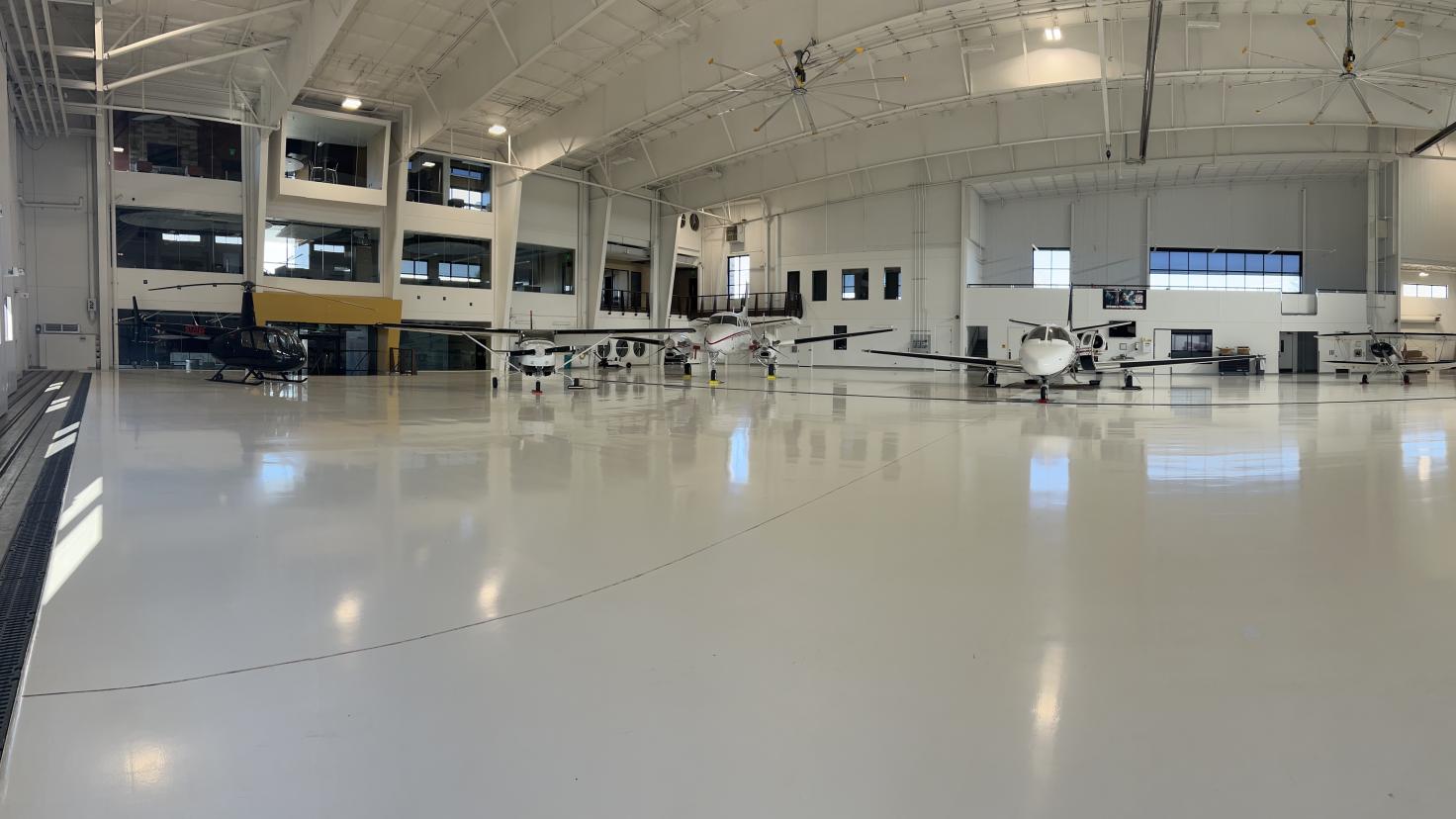 panoramic inside of airplane hangar with white shiny floor and 3 airplanes