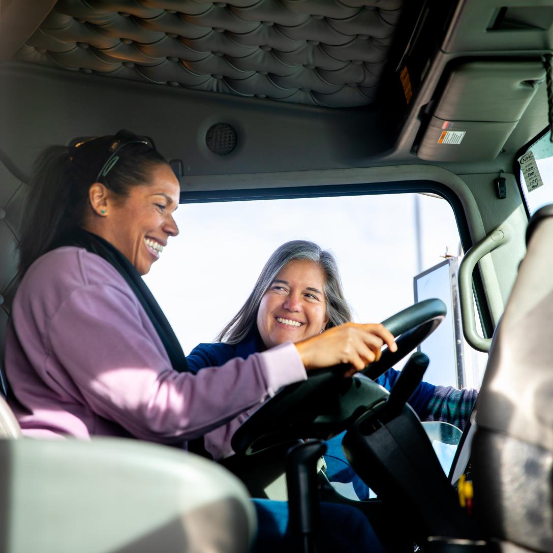 Female instructor instructing another woman behind the wheel of a a semi truck