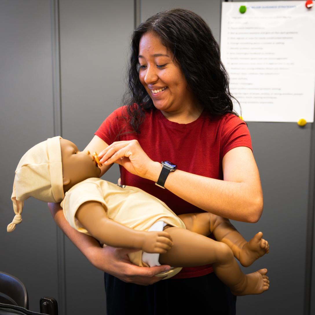 Early Childhood Education Student holds robotic infant at puts pacifier in its mouth