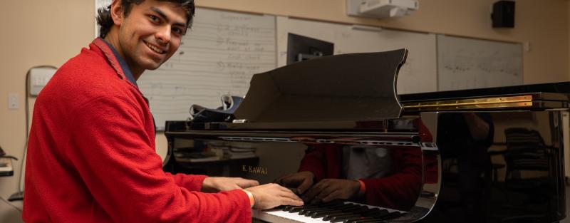 An Aims music student seated at a piano while smiling at the camera