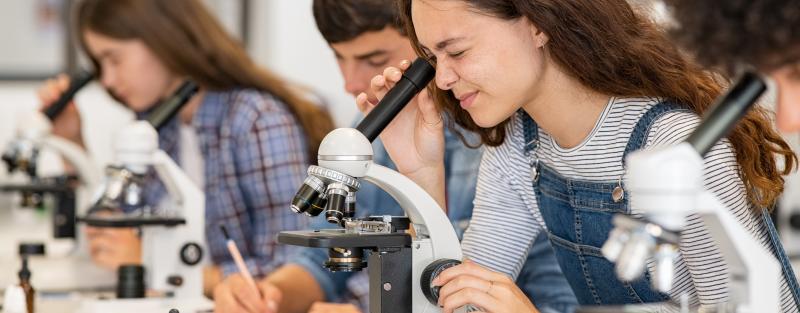 A group of biology students looking through microscopes in a lab class