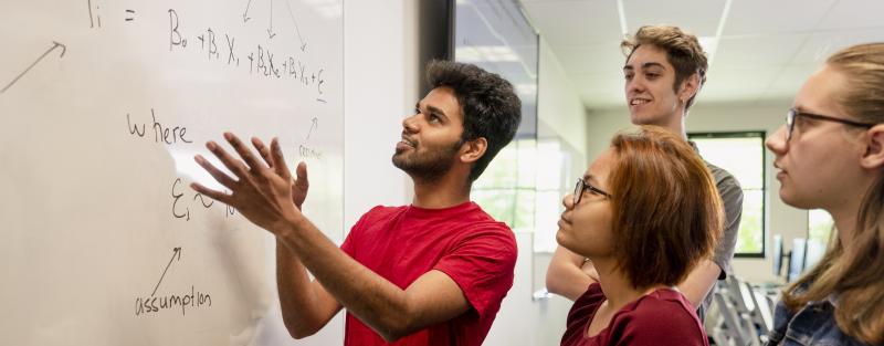 Students standing at a whiteboard working together on a math problem