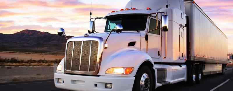 semi truck driving out of sunset with sky reflection on its side