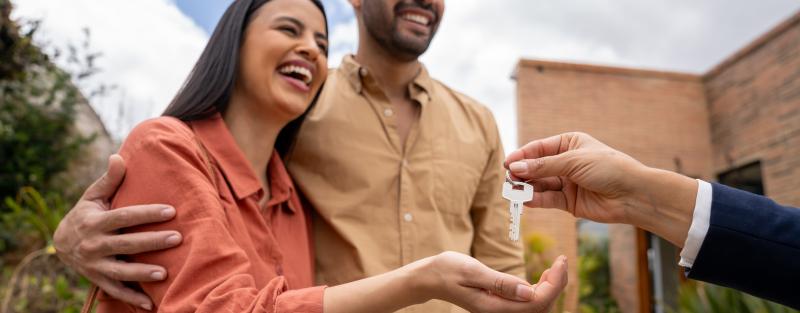 A couple standing in front of house receiving key to their new home