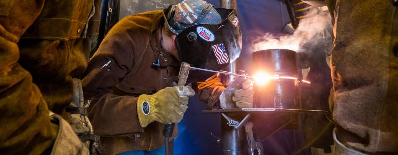 Aims welding students wearing safety masks and gear practicing welding