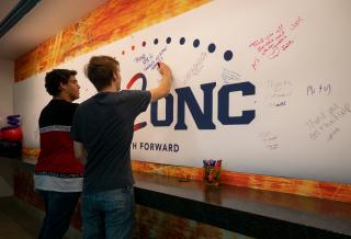 2 male Aims2UNC transfer students writing on the banner wall at transitions day