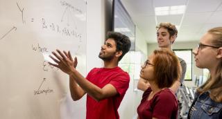 Students standing at a whiteboard working together on a math problem