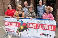 Group standing in front of sign saying, "Welcome Aims Alumni."