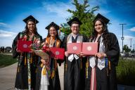 4 students with diplomas after graduation in caps and gowns