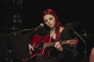 female on stages playing guilar in front of a microphone