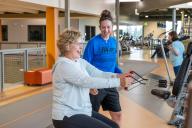 An Aims personal trainer helping a person to use exercise equipment at the PERC
