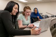 three students looking at a laptop in a classroom